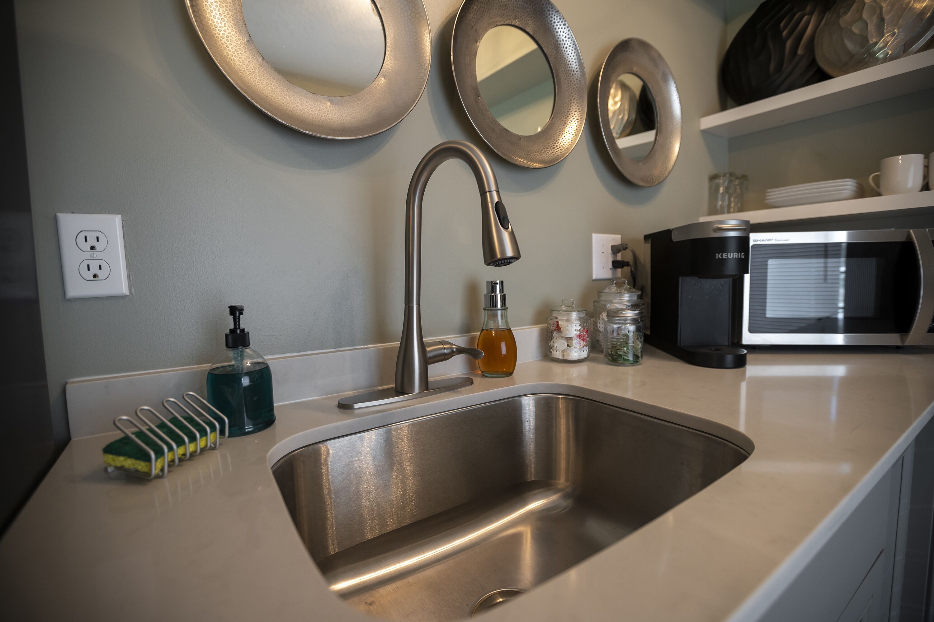 A modern kitchen with a stainless steel sink, a coffee maker, and decorative mirrors on the wall.