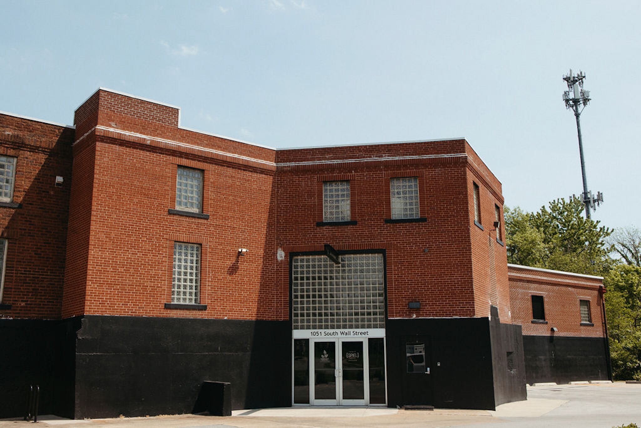 Un edificio de ladrillo rojo con un amplio acceso por puerta de vidrio, fachada inferior negra y un letrero que dice '1051 South Wall Street'.