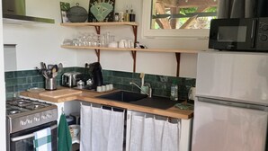 A compact kitchen with a gas stove, oven, microwave, and a sink. There are shelves above the counter holding various kitchen items, and a window above the sink. - Studio*** 2 People Heated swimming pool between Châteaux de la Loire and Futuroscope (Rilly-sur-Vienne)