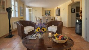 Un salon avec deux canapés en cuir, une table basse avec des livres et un vase de fleurs, ainsi qu’un panier de fruits.
