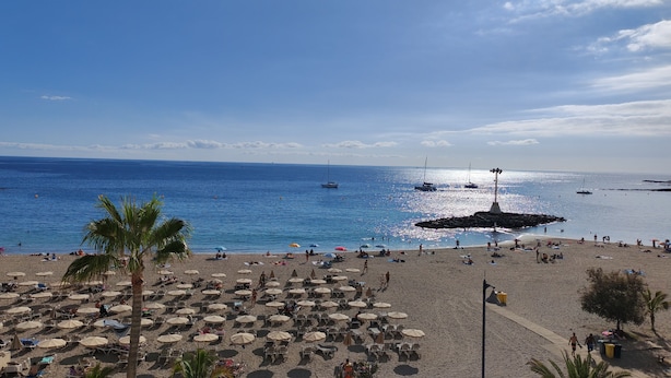 A beach with rows of sun loungers and umbrellas, a rocky breakwater, and boats in the water. - Azahara III Studio, Playa Las Vistas with wonderful seaview (Playa de la Américas)