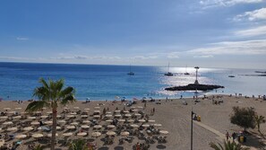 A beach with rows of sun loungers and umbrellas, a rocky breakwater, and boats in the water. - Azahara III Studio, Playa Las Vistas with wonderful seaview (Playa de la Américas)