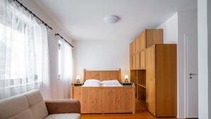 A bedroom with a wooden bed, two bedside tables with lamps, a wooden wardrobe, and a sofa. - Cozy pension Sonnenhaus (Gundersheim)