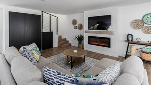 Una sala de estar moderna con chimenea, un conjunto de sofás, una mesa de centro y un televisor montado sobre la chimenea.