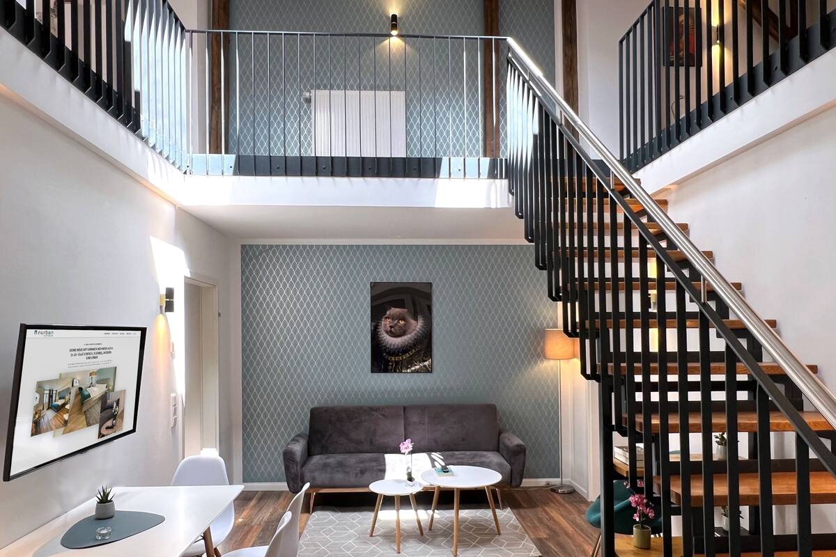 Un intérieur moderne avec un escalier, un mur gris à motifs, un canapé gris, une table à manger et un tableau encadré.