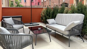 A patio area with a grey wicker sofa, two grey wicker chairs, a glass coffee table, and a large black umbrella. - Nurban Apartments City 2 (Nuremberg)