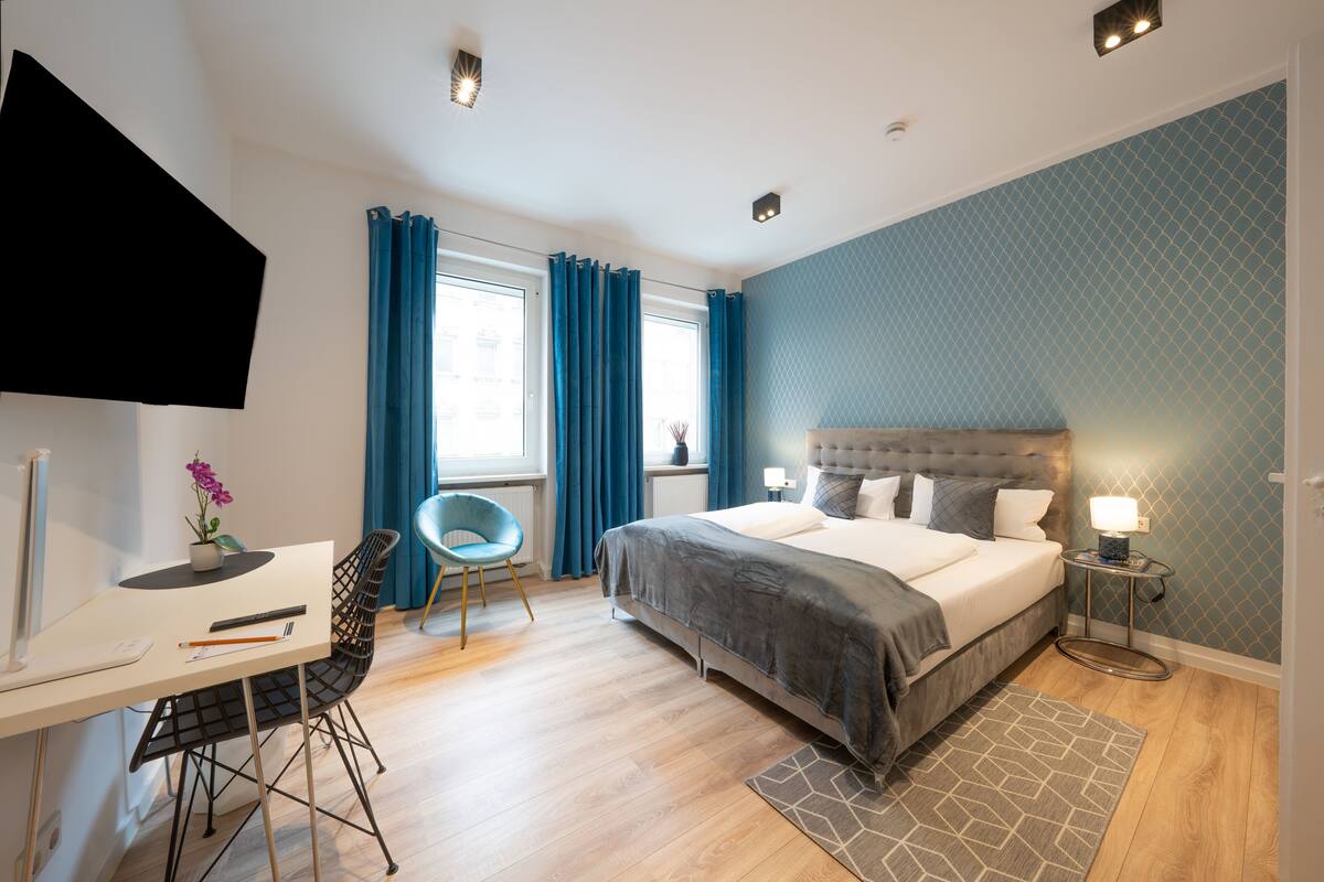 Une chambre à coucher moderne, équipée d’un lit, d’un bureau, d’une chaise et d’un téléviseur fixé au mur.