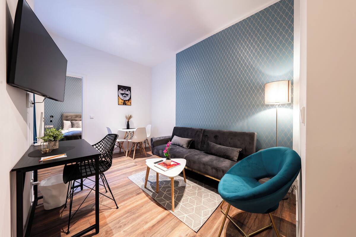 Un salon moderne avec un canapé, un fauteuil bleu, une table basse et un téléviseur fixé au mur.