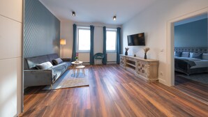 A modern living room with a sofa, a small table, and a TV mounted on the wall. - Nurban Apartments City 2 (Nuremberg)