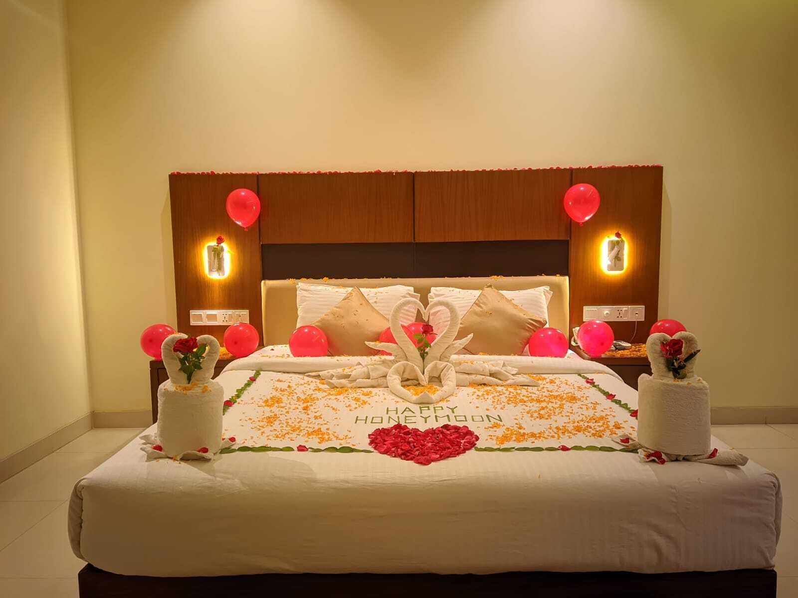 A hotel room with a bed adorned with a 'Happy Honeymoon' message, red balloons, and decorative swans made of towels.