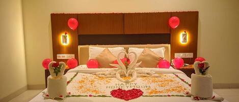 A hotel room with a bed adorned with a 'Happy Honeymoon' message, red balloons, and decorative swans made of towels.