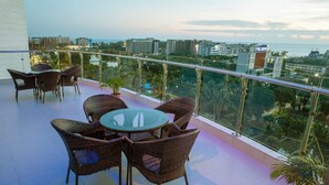 Eine Dachterrasse mit Korbmöbeln, einem Glastisch und Blick auf Stadt und Meer.