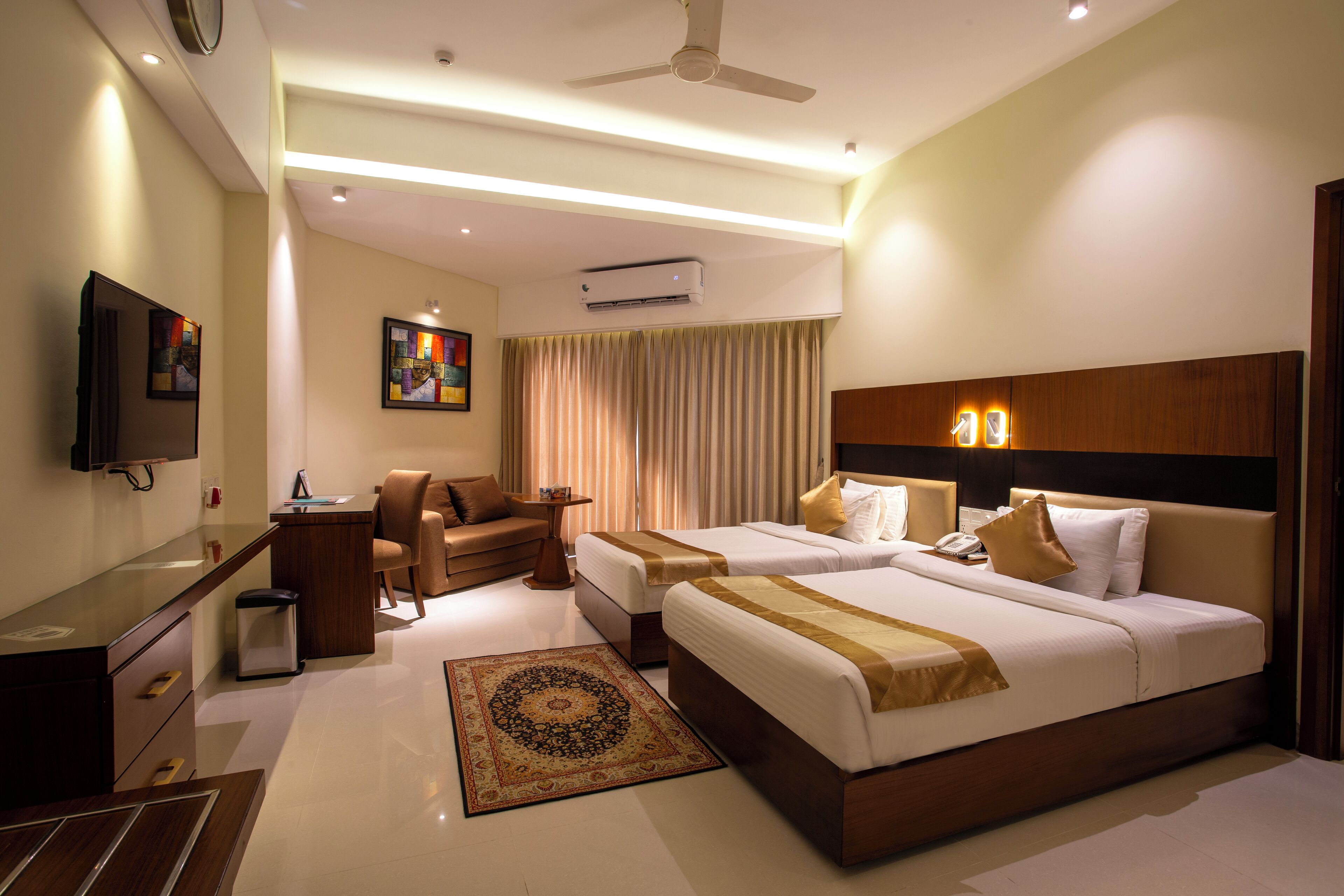 A hotel room with two beds, a desk, a chair, a TV, and an air conditioning unit.