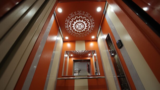 Un ascensor moderno con diseño geométrico en el techo y pared espejada.