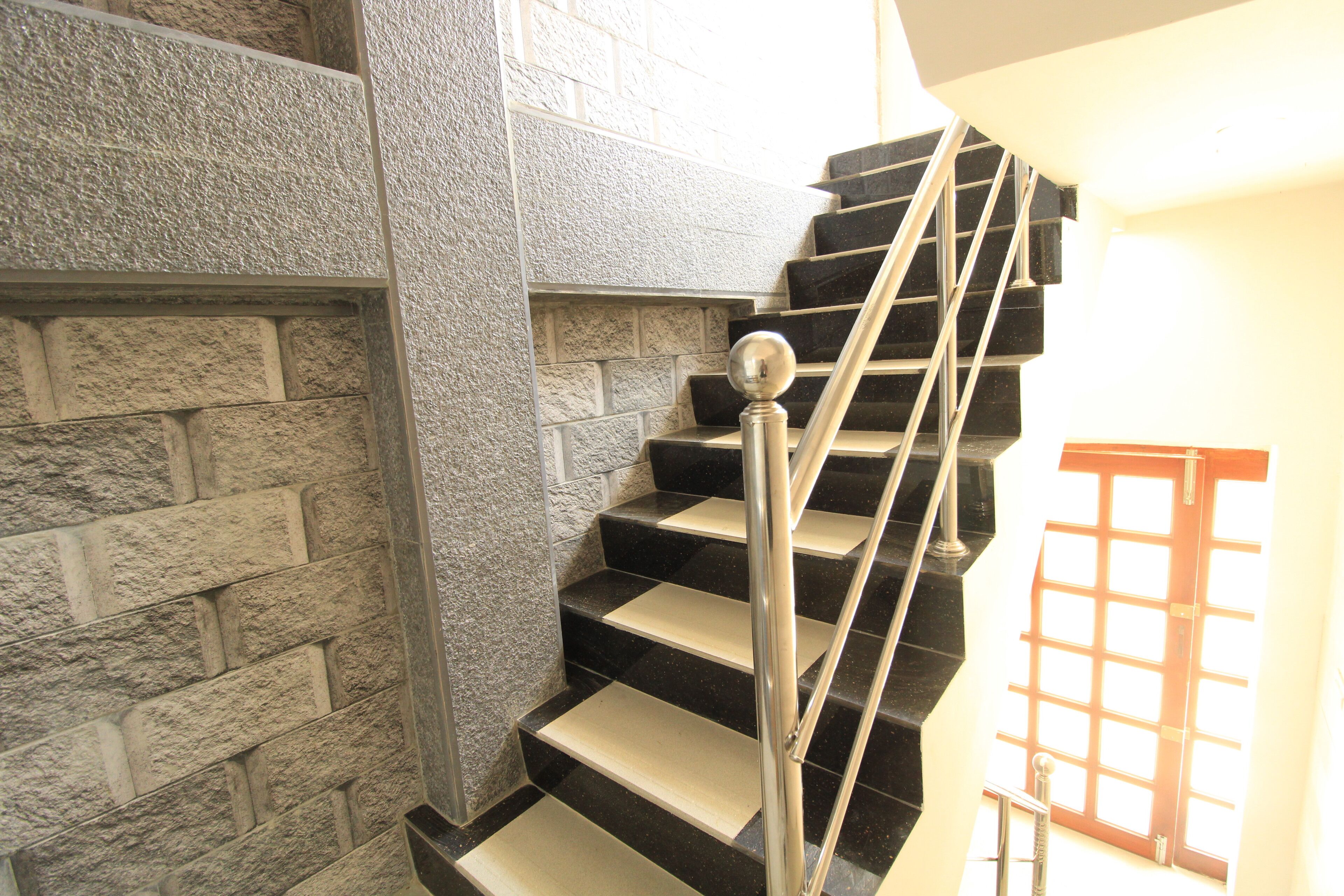 A staircase with black steps and a metal handrail, leading to a landing with a window.
