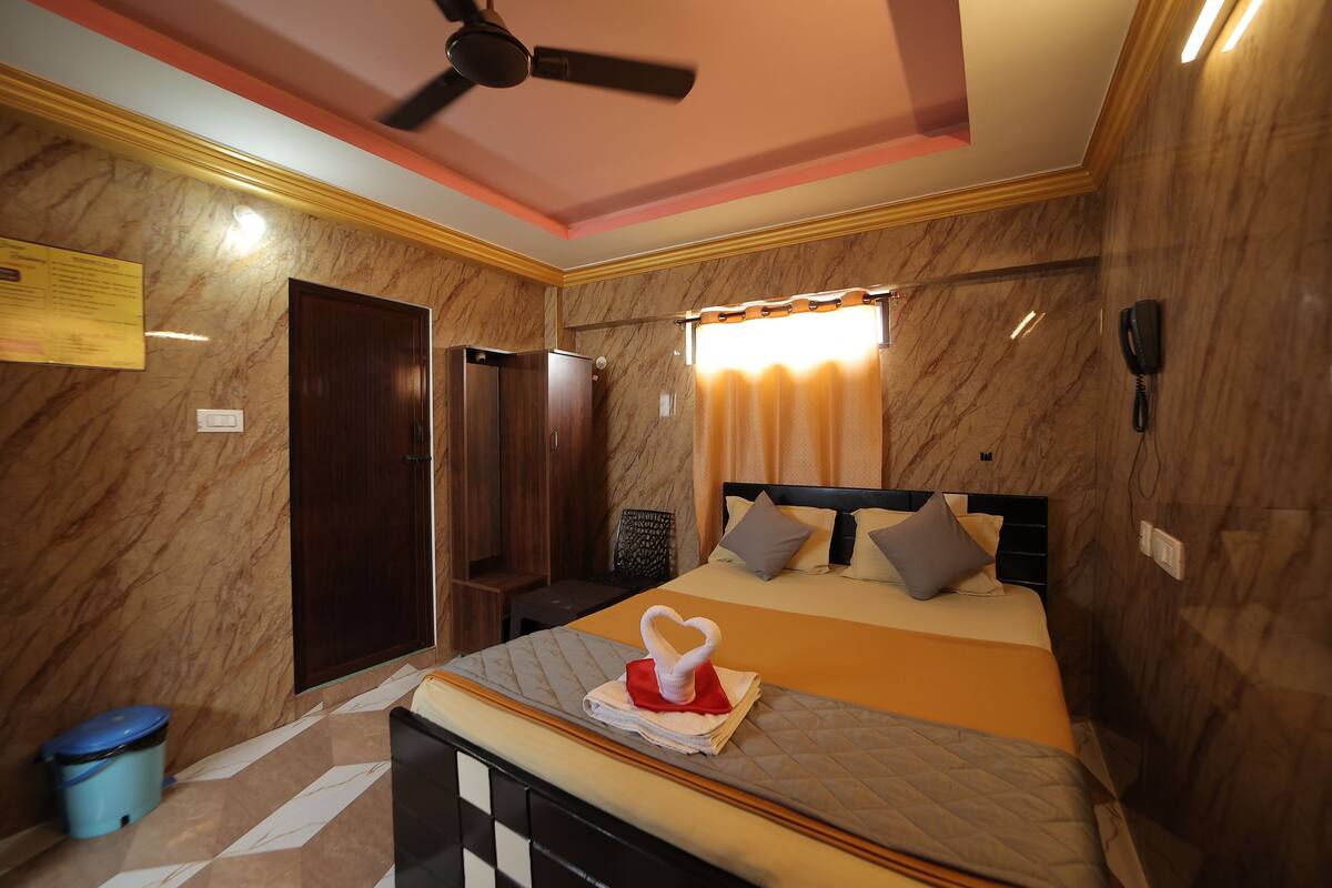 A hotel room with a bed, a ceiling fan, a telephone, and a window with curtains.