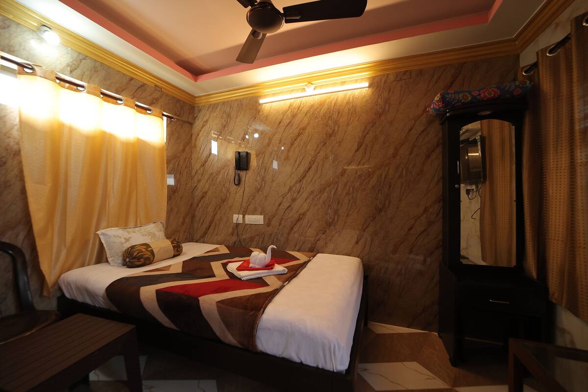 A hotel room with a bed, a desk, a mirror, and a ceiling fan.