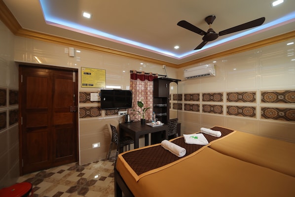 Una habitación de hotel con cama, escritorio, televisor y ventilador de techo.