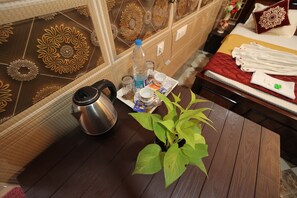 Een houten tafel met een waterfles, een waterkoker en een dienblad met kopjes en lekkernijen.