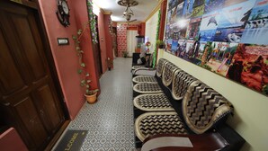 Un pasillo con piso estampado, un felpudo, un banco con cojines de asiento tejidos, una pared con cuadros enmarcados y una puerta con la etiqueta 'ROOM'.