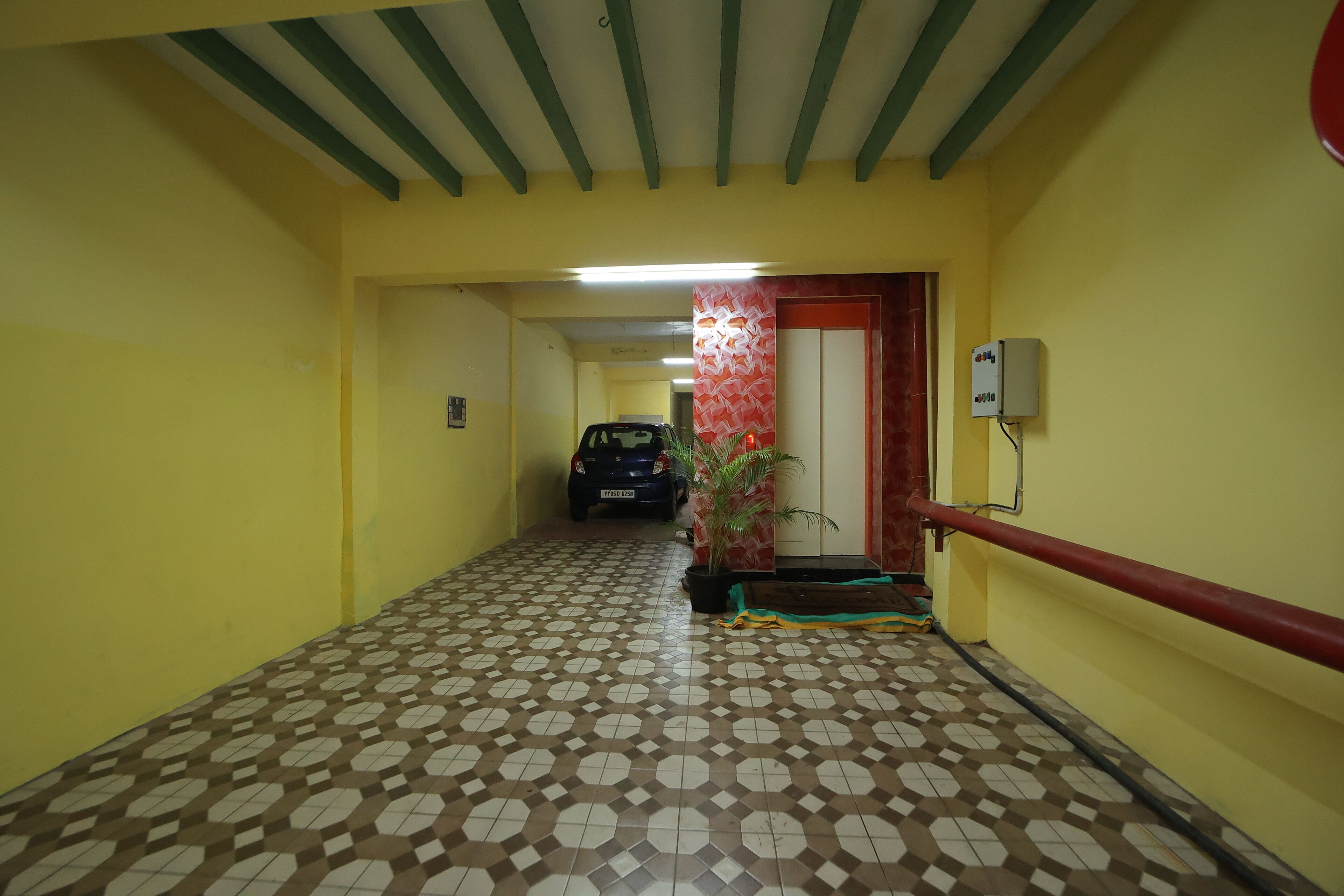 A hallway with patterned flooring, a parked car, a potted plant, and a wall-mounted electrical box.