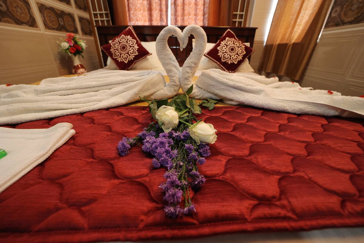 A bed with towels arranged in a heart shape, a bouquet of flowers, and decorative pillows.