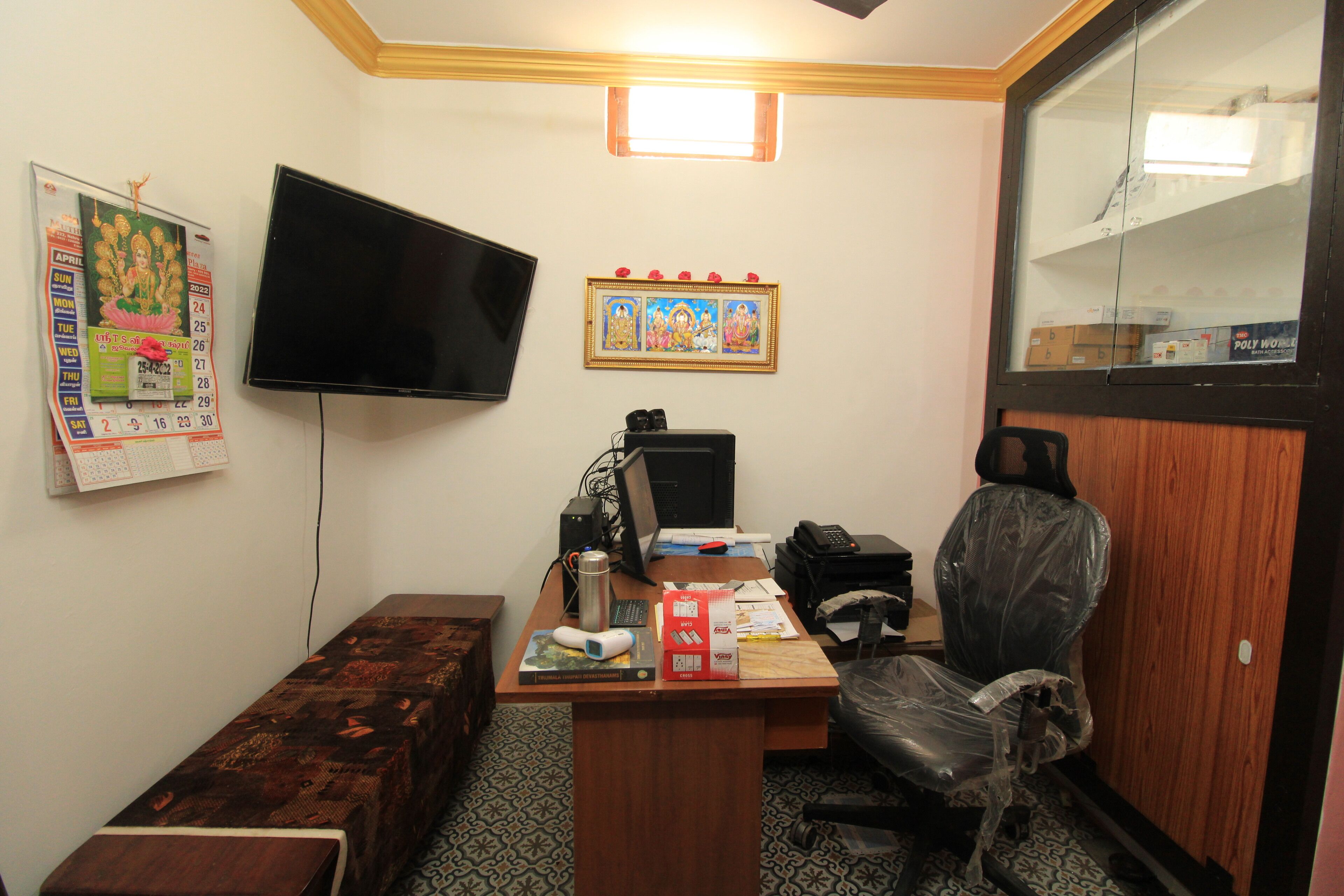 A small office with a desk, computer, chair, and a TV mounted on the wall.