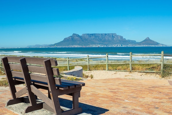A bench overlooking a beach with a view of a mountain and the ocean. - Big Bay Beach Club 21 (Cape Town)
