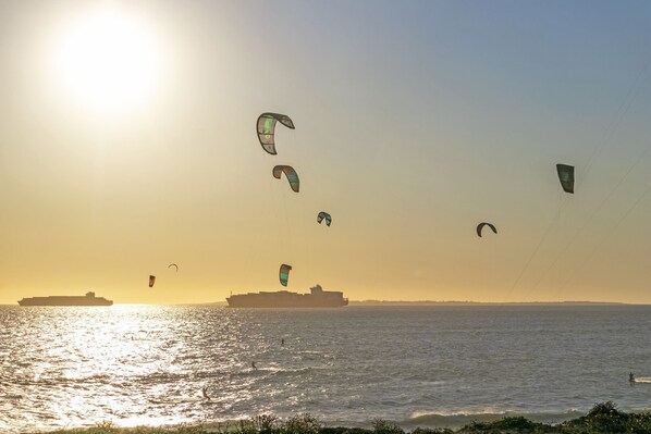 A sunset over a body of water with multiple kites and a large ship in the distance.