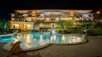 Un hôtel moderne doté d’une piscine, de chaises longues et d’un espace extérieur bien éclairé la nuit.