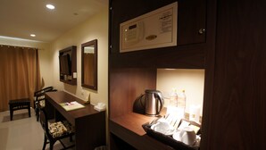 Habitación de hotel con escritorio de madera, cafetera, botella de agua y cubo de basura.
