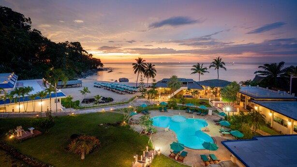 Un resort con piscina, sillas de descanso y vista al océano al atardecer.