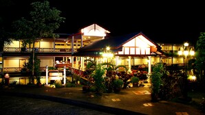 Un hotel de varios pisos con un área exterior cubierta, plantas en macetas y una entrada bien iluminada.
