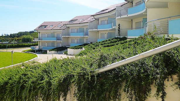 Un hotel de varios pisos con balcones, piscina y un jardín bien cuidado.