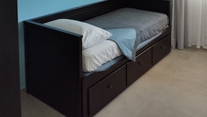 Un dormitorio con una cama individual, cabecera oscura, lámpara colgante y ventana con cortinas.