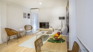 A modern living room with a sofa, a coffee table with fruit, wicker chairs, a TV, and a white door. - Apartamento Interior, 1 Dormitorio 1 Baño (Malasaña)