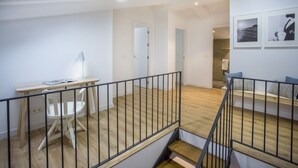 A spacious room with a wooden floor, a desk with a chair, and a staircase with a railing. - Apartamento Exterior Duplex 4 Dormitorios 2 Baños (Malasaña)