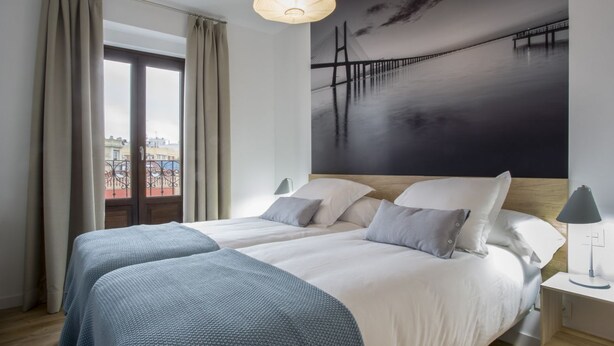 A hotel room with two beds, a large window with curtains, a painting of a bridge, and a nightstand with a lamp. - Apartamento Exterior Duplex 4 Dormitorios 2 Baños (Malasaña)