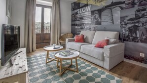 A living room with a sofa, two side tables, a television, and a large wall mural. - Apartamento Exterior Duplex 4 Dormitorios 3 Baños (Malasaña)