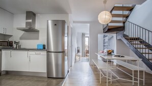 A modern kitchen with stainless steel appliances, a dining area with a white table, and a staircase. - Apartamento Exterior Duplex 4 Dormitorios 3 Baños (Malasaña)
