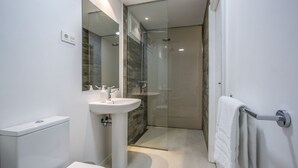 A modern bathroom with a glass-enclosed shower, a pedestal sink, and a toilet.