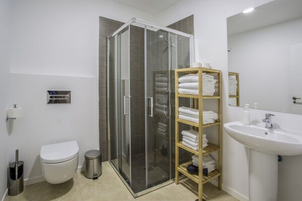 Une salle de bain moderne avec une douche à parois de verre, des toilettes, un lavabo et une étagère où sont soigneusement pliées des serviettes.