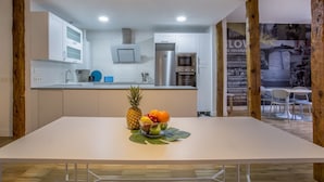 A modern kitchen with white cabinets, a stainless steel refrigerator, and a dining area with a white table and chairs.