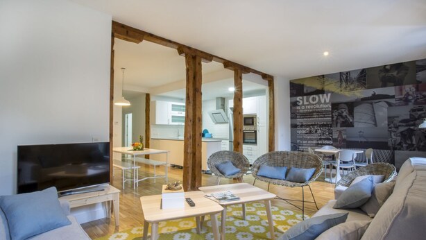 A modern living room with a flat-screen TV, sofas, a coffee table, and wicker chairs.