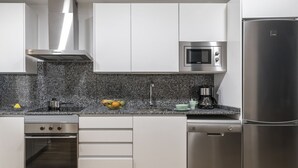 A modern kitchen with white cabinets, a granite countertop, a stainless steel oven, a microwave, a coffee maker, and a dishwasher.