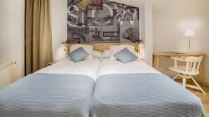 Ein Doppelbett mit zwei Kissen, ein Holztisch, ein Stuhl und eine Wand mit einer Collage aus Schwarz-Weiß-Fotos.