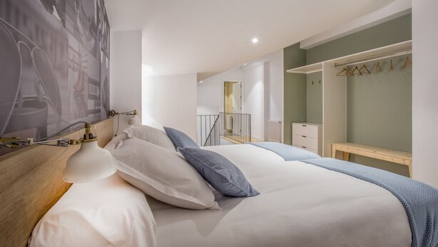A modern bedroom with a large bed, bedside table, and a wall-mounted lamp. - Apartamento Interior Duplex 1 Dormitorio 2 Baños (Malasaña)