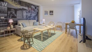 A modern living room with a sofa, coffee table, and chairs. There is a large wall art piece, a lamp, and a small table with decorative items. - Apartamento Interior Duplex 1 Dormitorio 2 Baños (Malasaña)