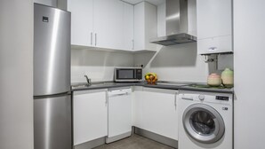 A compact kitchen with a stainless steel refrigerator, a microwave, a dishwasher, and a washing machine. - Apartamento Exterior Superior de 2 Dormitorios 1 Baño (Malasaña)