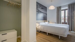 A bedroom with a bed, a bedside table, a hanging wardrobe, and a large window with curtains. - Apartamento Exterior Superior de 2 Dormitorios 1 Baño (Malasaña)